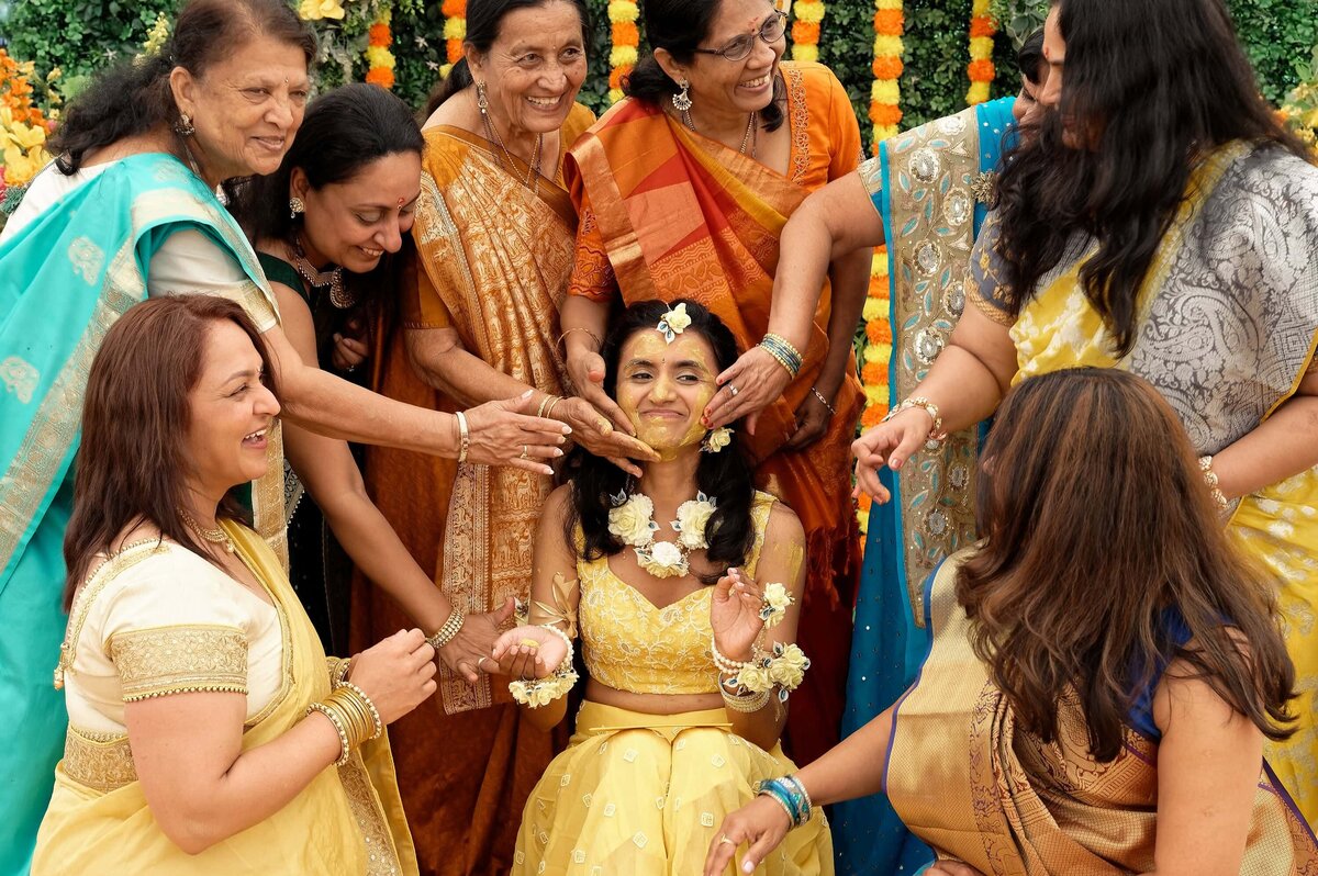 Indian bride having yellow dye smeared on her face by her female close family members