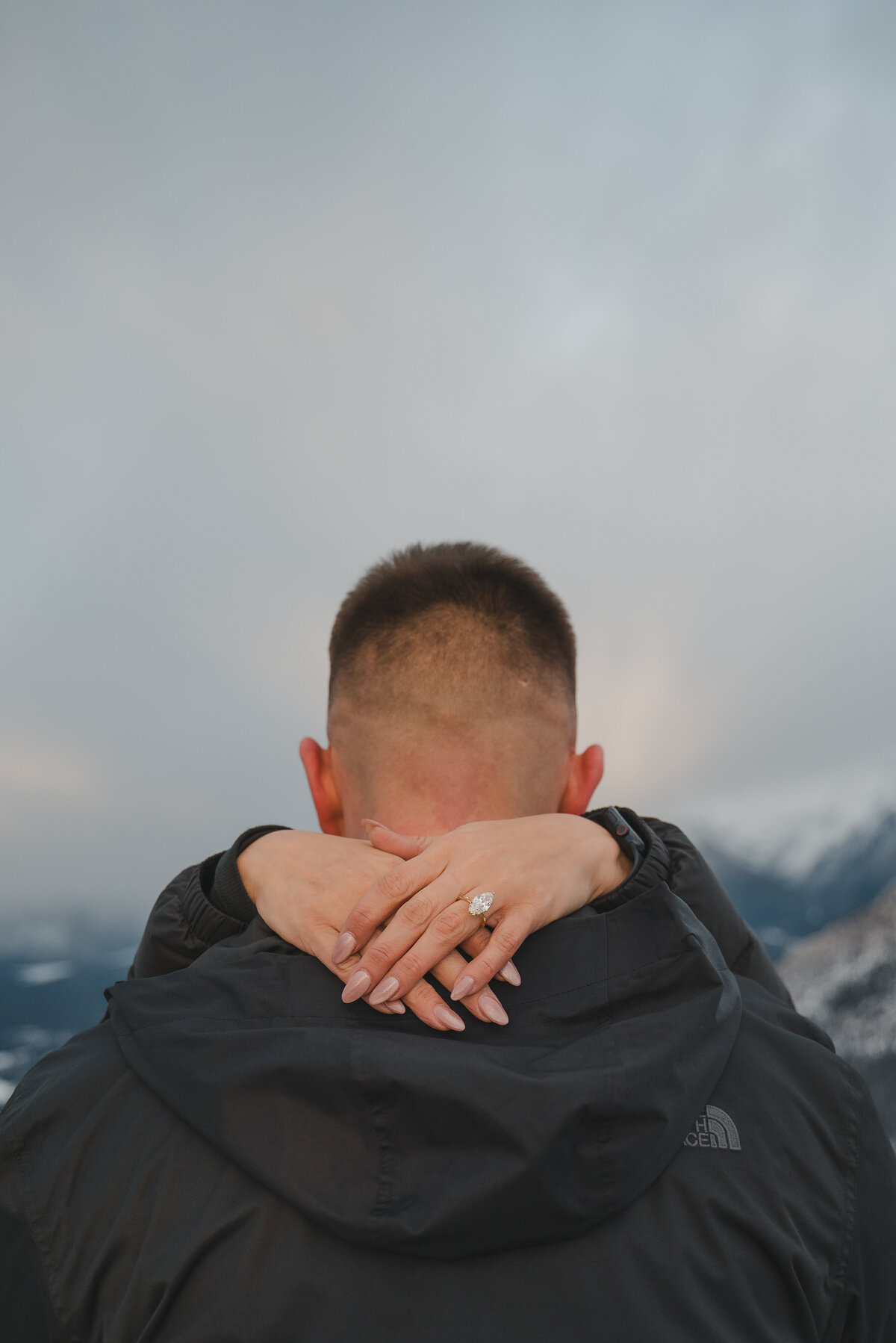 Woman shows off engagement ring over partner’s shoulder during proposal in Banff.