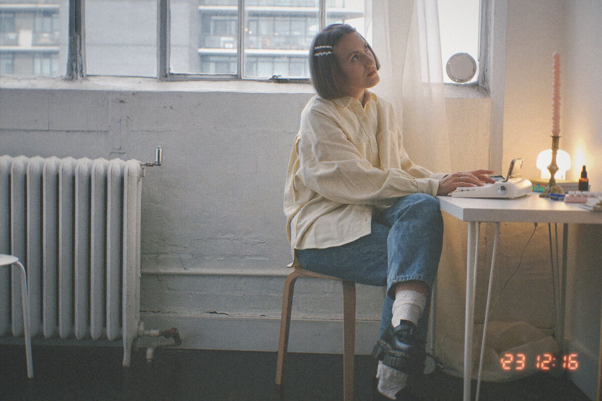 Margarita sits at her desk, writing website copy as she gazes out into space, brainstorming crative ideas. A white radiator and big loft windows are in the backdrop.