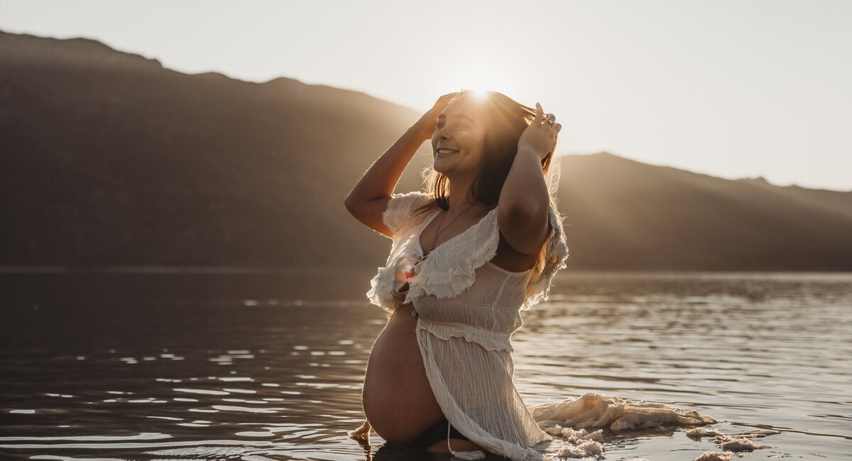 pregnant woman standing in the water posing for her maternity photography session in wanaka