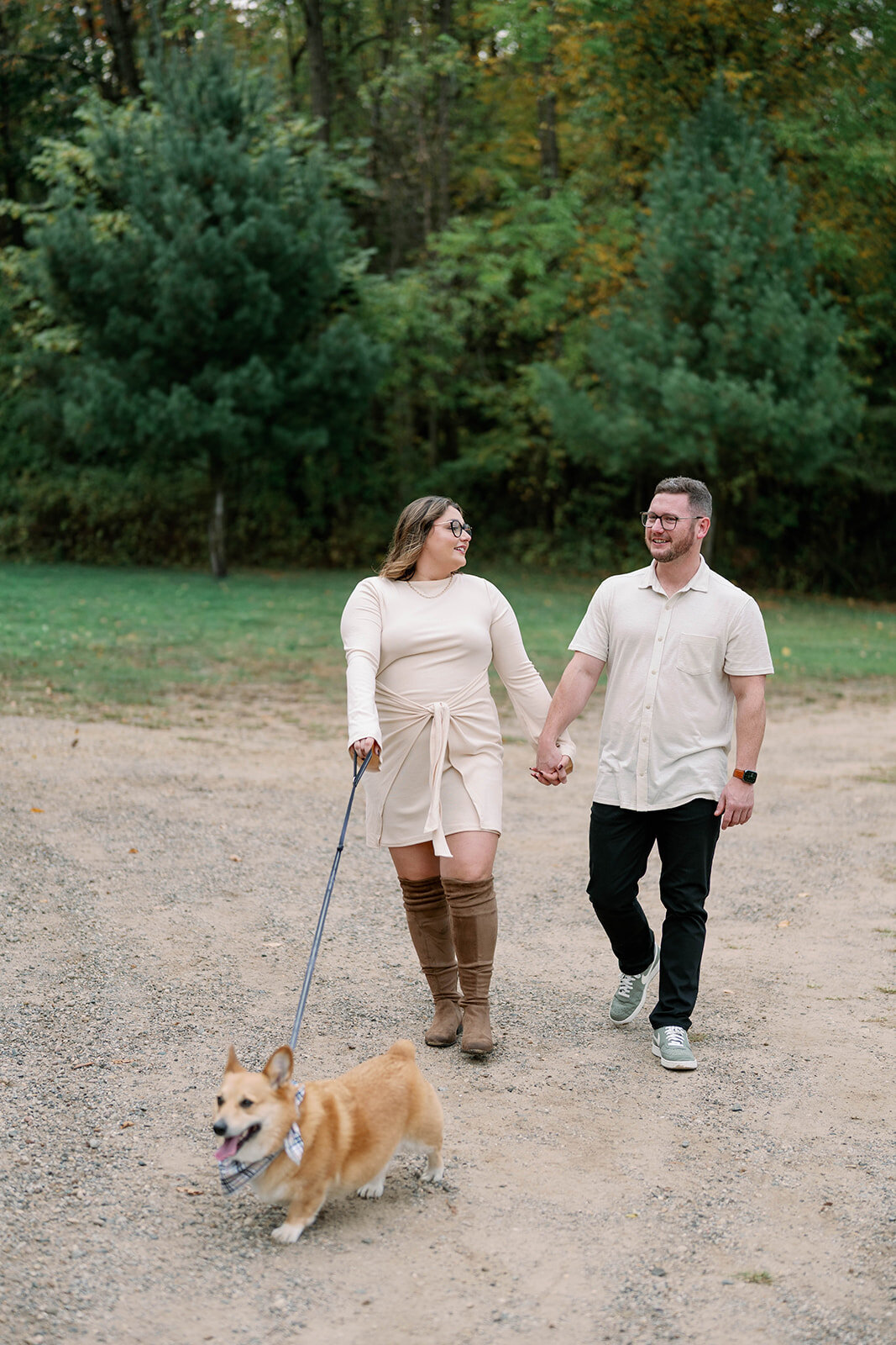 Couple walking with their dog along a wooded trail during their Michigan engagement session at Al Sabo Preserve.