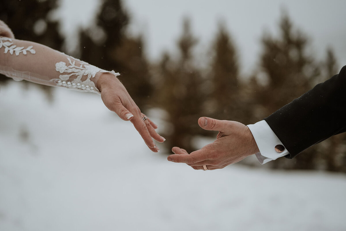 Bride and groom reach toward each other in snowy Breckenridge landscape.