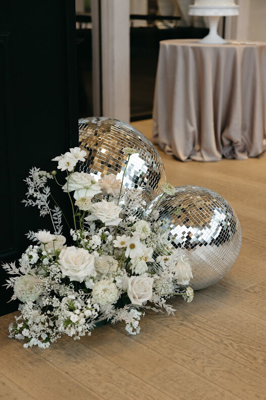 An airy floral arrangement enhances the wedding decor beside disco balls on the floor at the National Arts Centre's O'Born Room, creating a chic atmosphere.