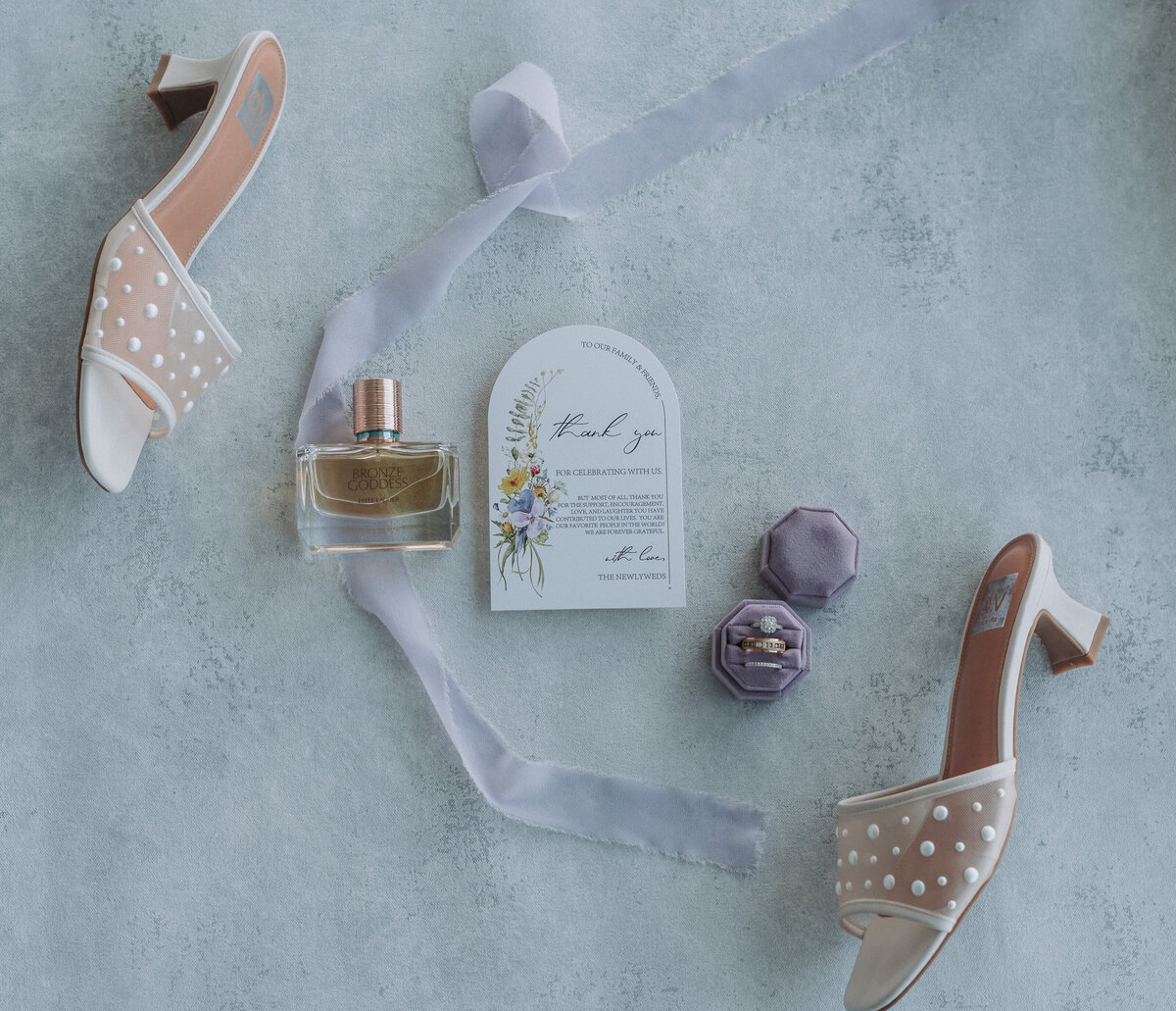 Flat lay with bridal shoes, thank you card, perfume, and ring box styled on a soft blue background at Lesner Inn.