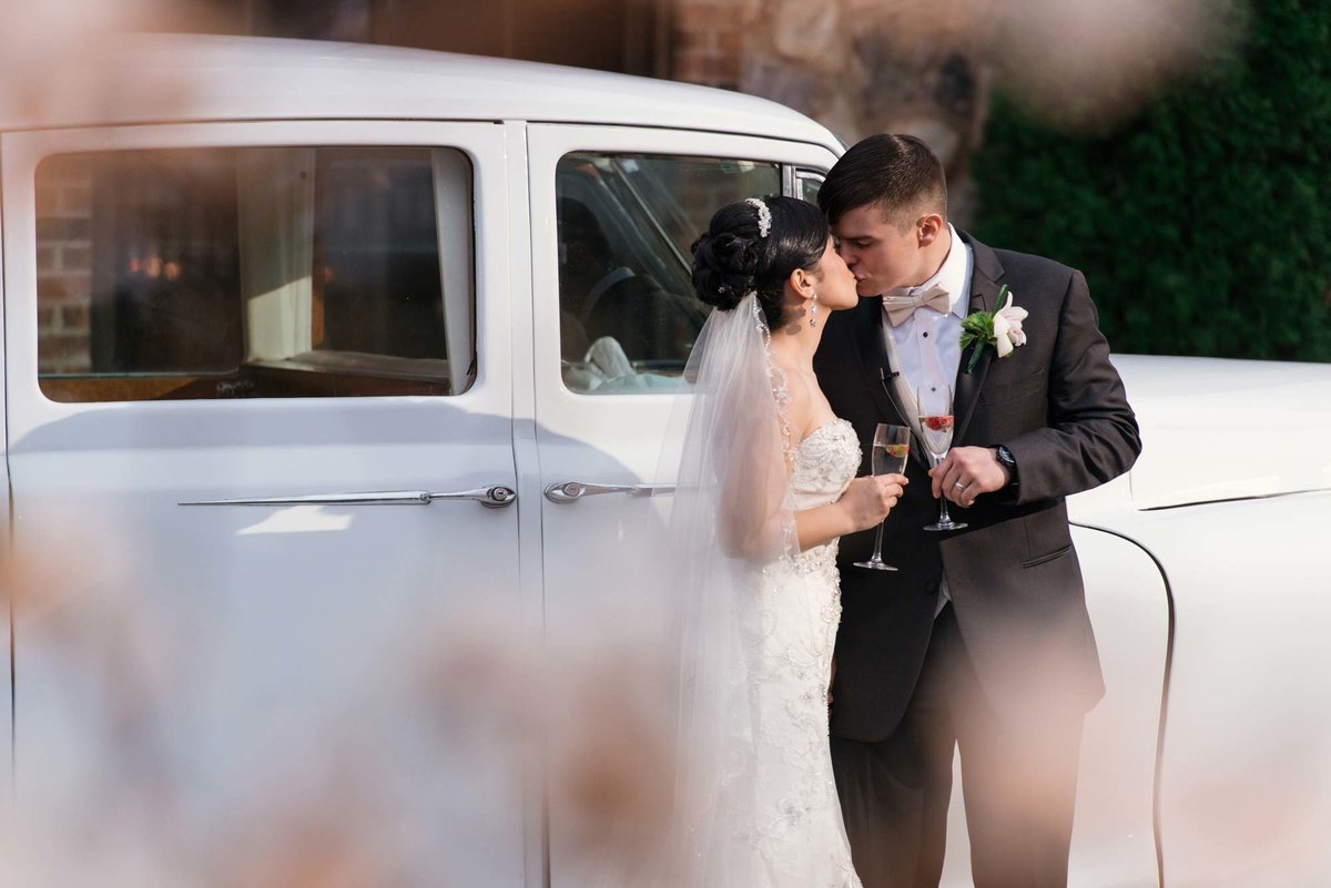 Bride and groom kissing next to their vintage car at Larkfield Manor