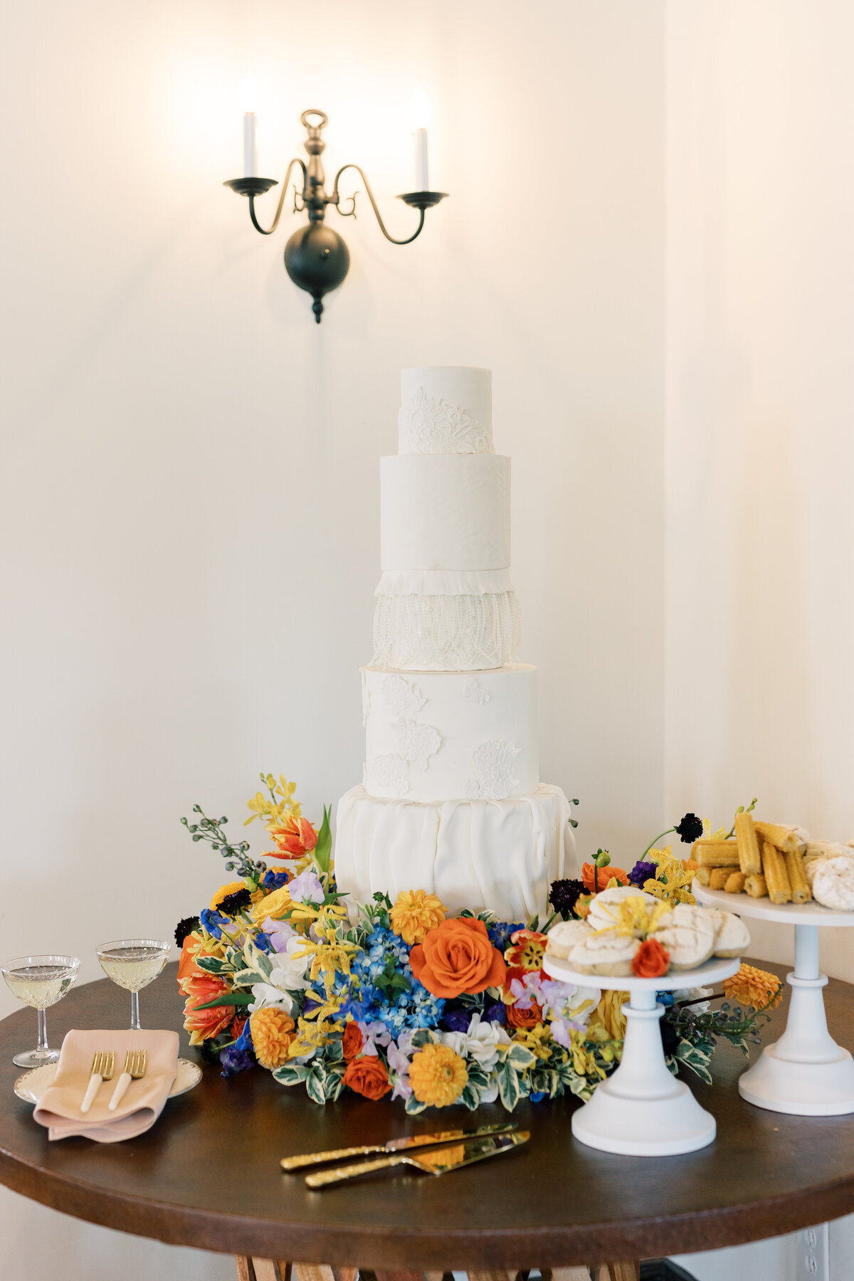 5 tier spanish inspired wedding cake with bright flowers surrounding it