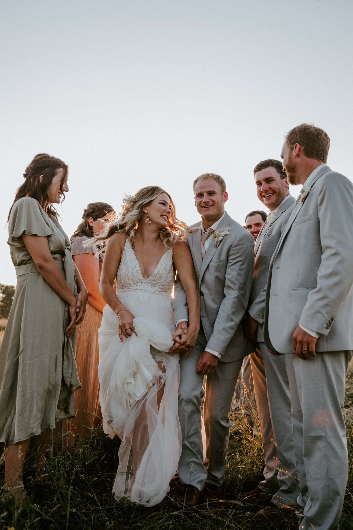 Bridesmaids and groomsmen form an aisle. Bride and groom walk between them smiling at each other at golden hour rustic barn wedding in Exeter, Ontario.