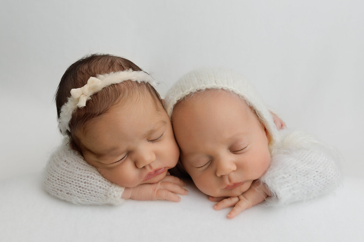 Brooklyn newborn twin photos. Twin girl and boy are sleeping on their bellies with their hand resting under their chin. Their heads are resting together. Babies are sleeping and wearing white knit onesies. Captured by premier Brooklyn NY newborn photographer Chaya Bornstein Photography.