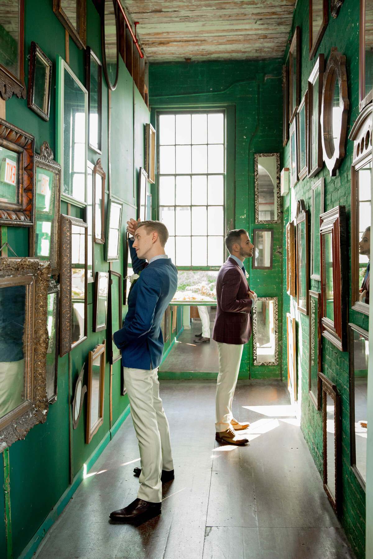 Two grooms standing in a hallway as the look at opposite walls.
