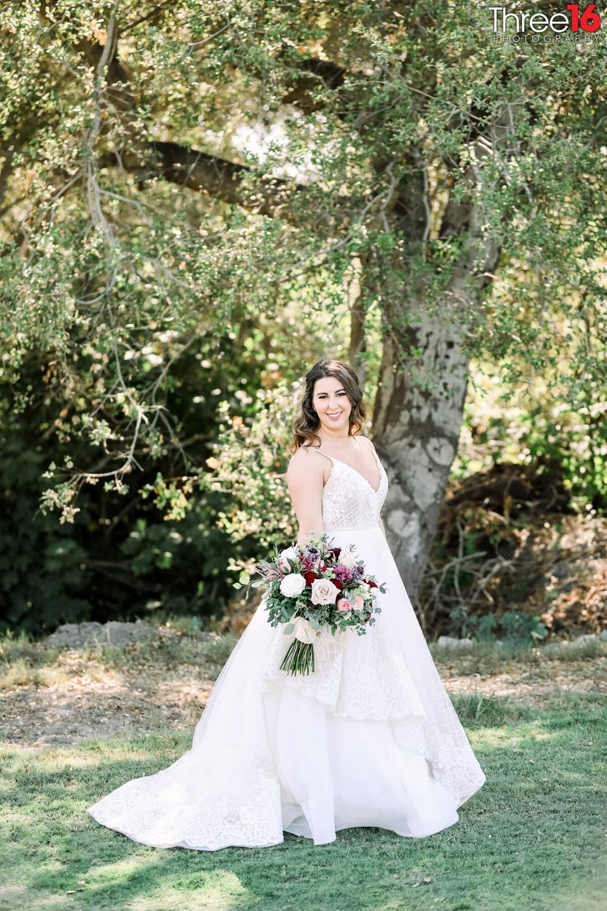 Bride poses with her bouquet under a very large tree