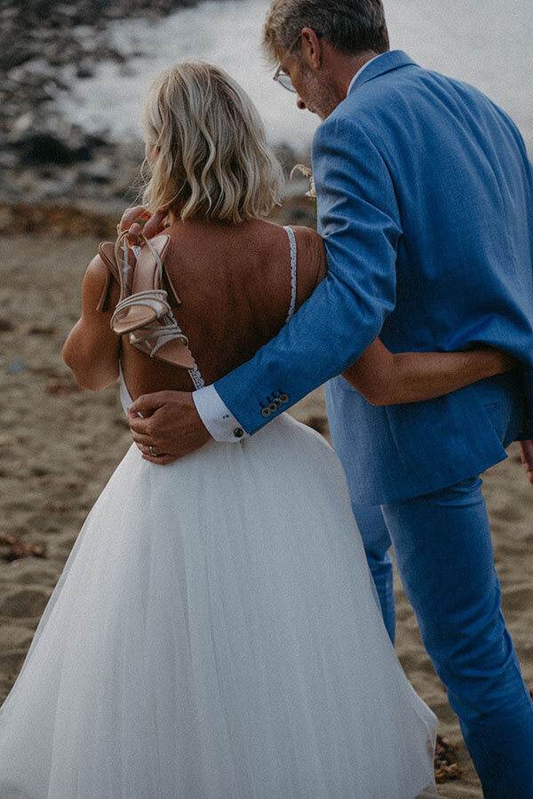 Les mariés s'éloignant bras dessus bras dessous, la mariée tient ses chaussures à la main. Un instant de complicité capturé en Bretagne par kamescop, vidéaste et photographe de mariage.