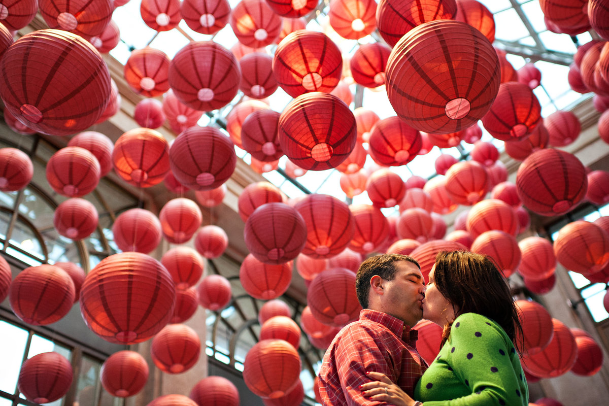 An engaged couple kiss under a paper lantern exhibit at longwood gardens in west chester, PA.
