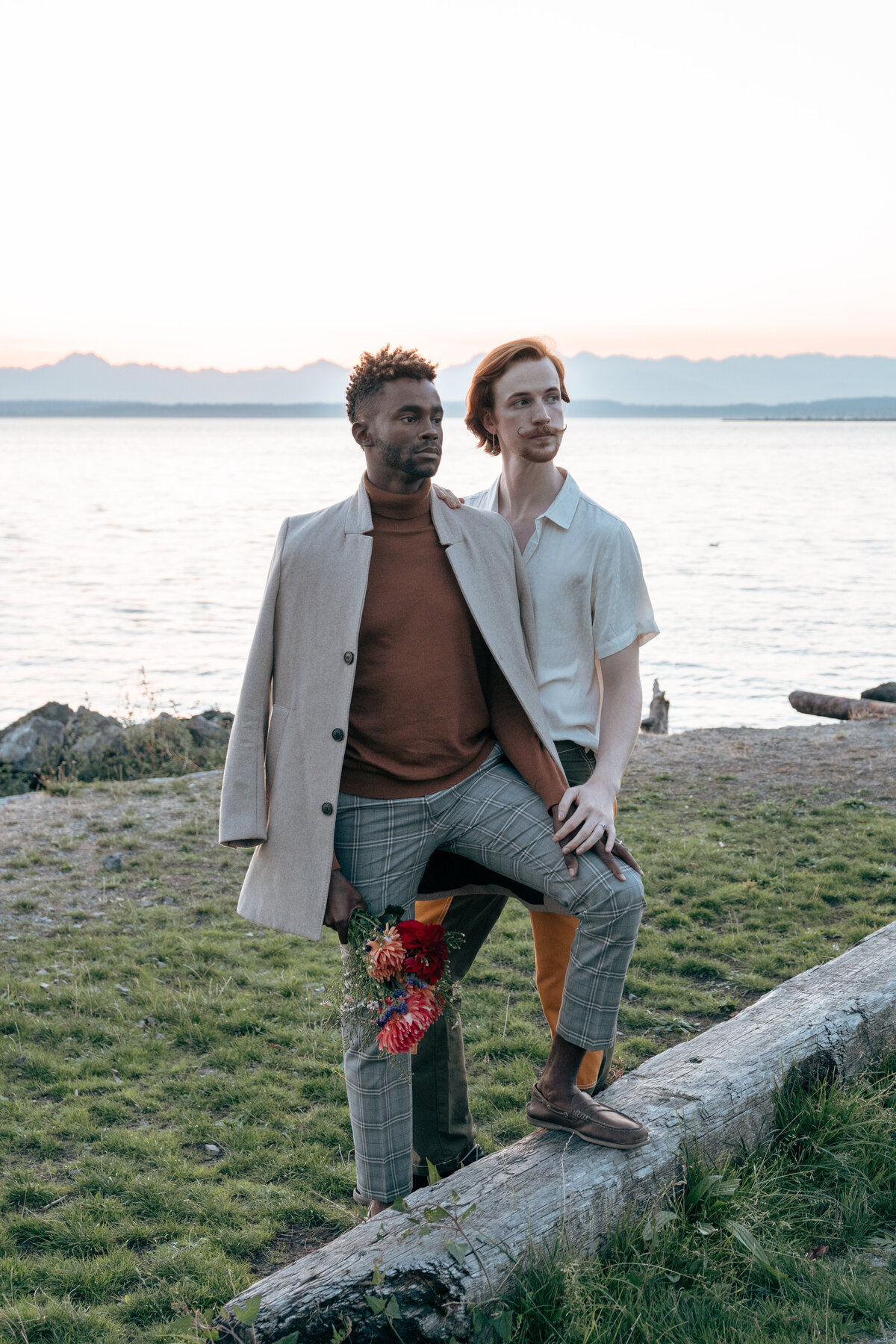 Queer couple at Pocket Beach in coastal Seattle during sunset, holding hands staring off into the distance