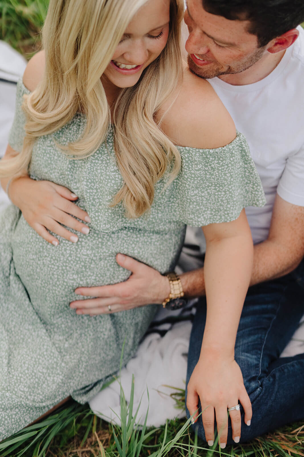 Couple sitting down with mans hand around baby bump for  maternity session in Finger Lakes, New York