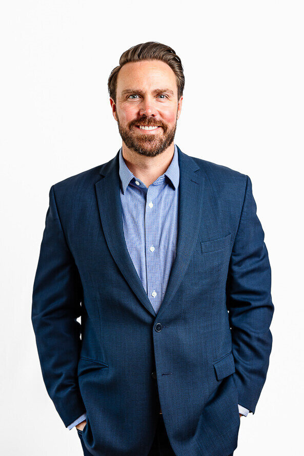 Man in blue jacket poses on white portable backdrop.