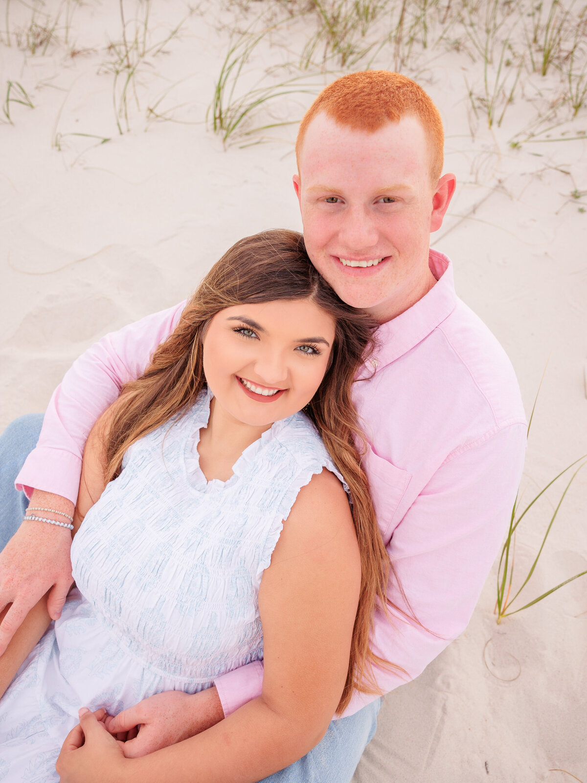 sweet embrace for young couple sitting in front of sand dunes.