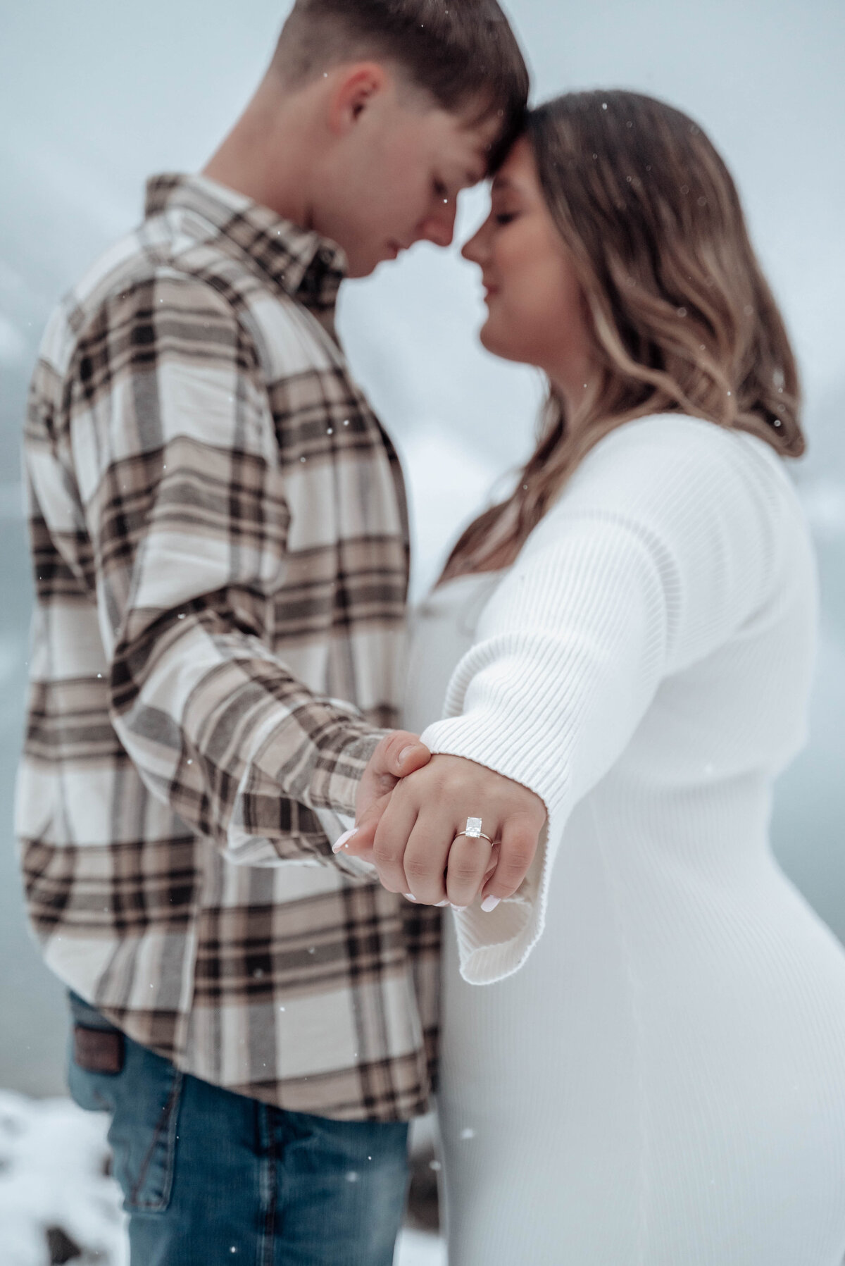 Close-up of couple holding hands showing off engagement ring in snow.