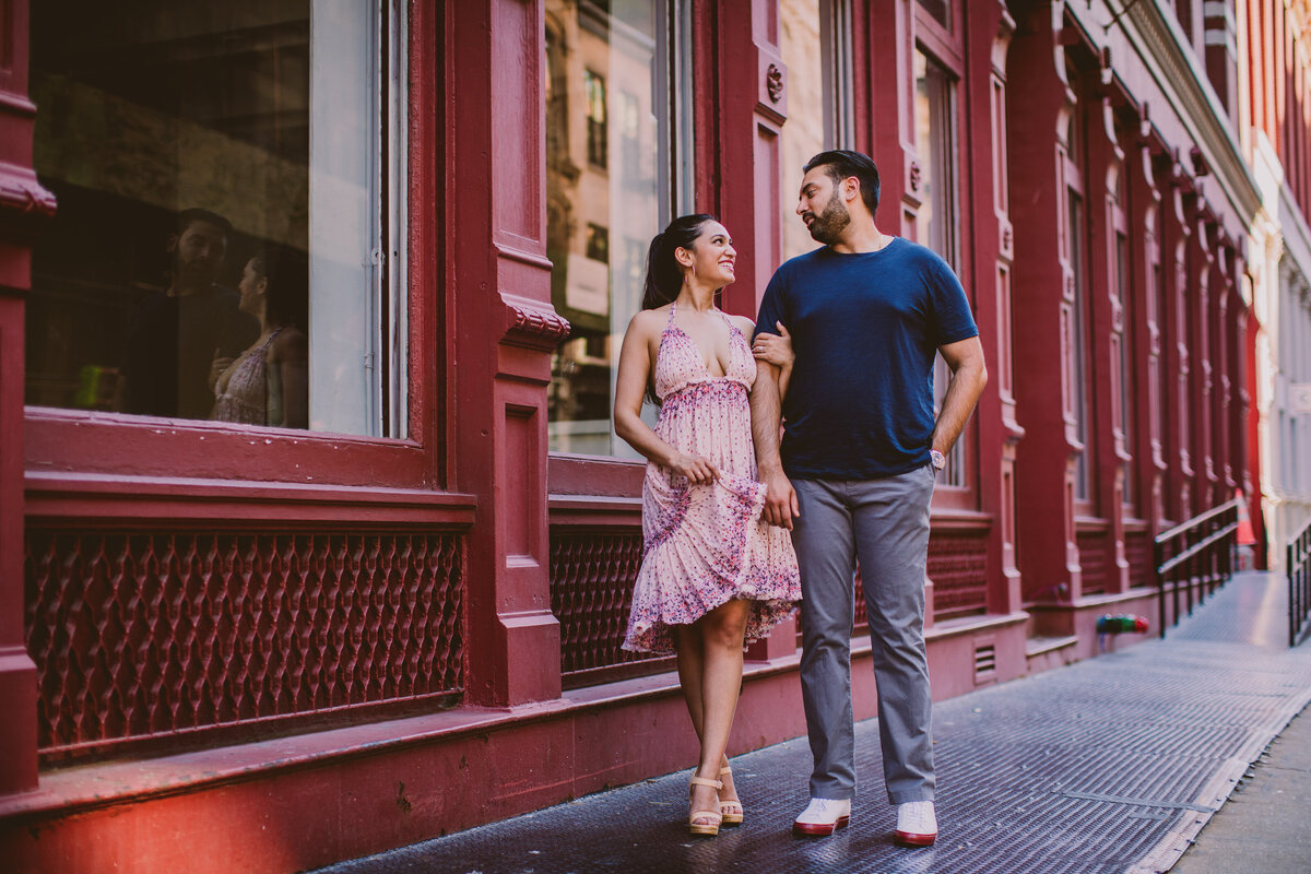 A couple smiling at each other in front of a red building in soho in nyc