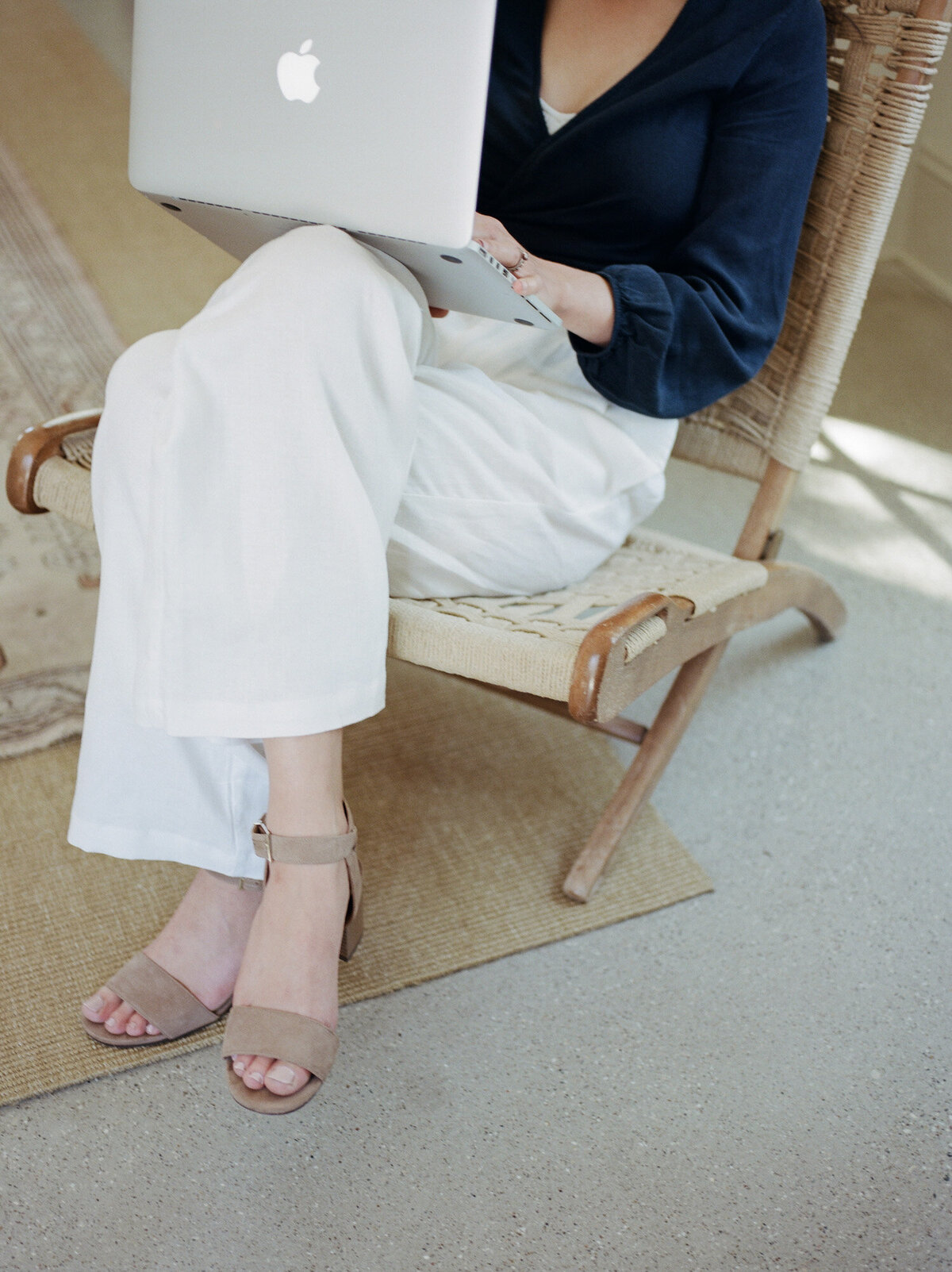 details of designer style, white pants, navy top, relaxing in chair with laptop, film brand photos