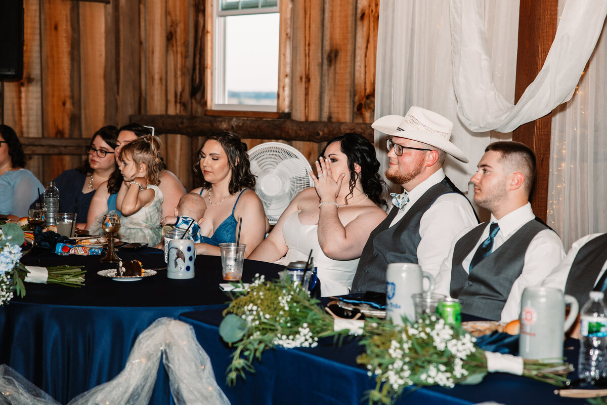A bride wipes a tear away at her head table during toasts