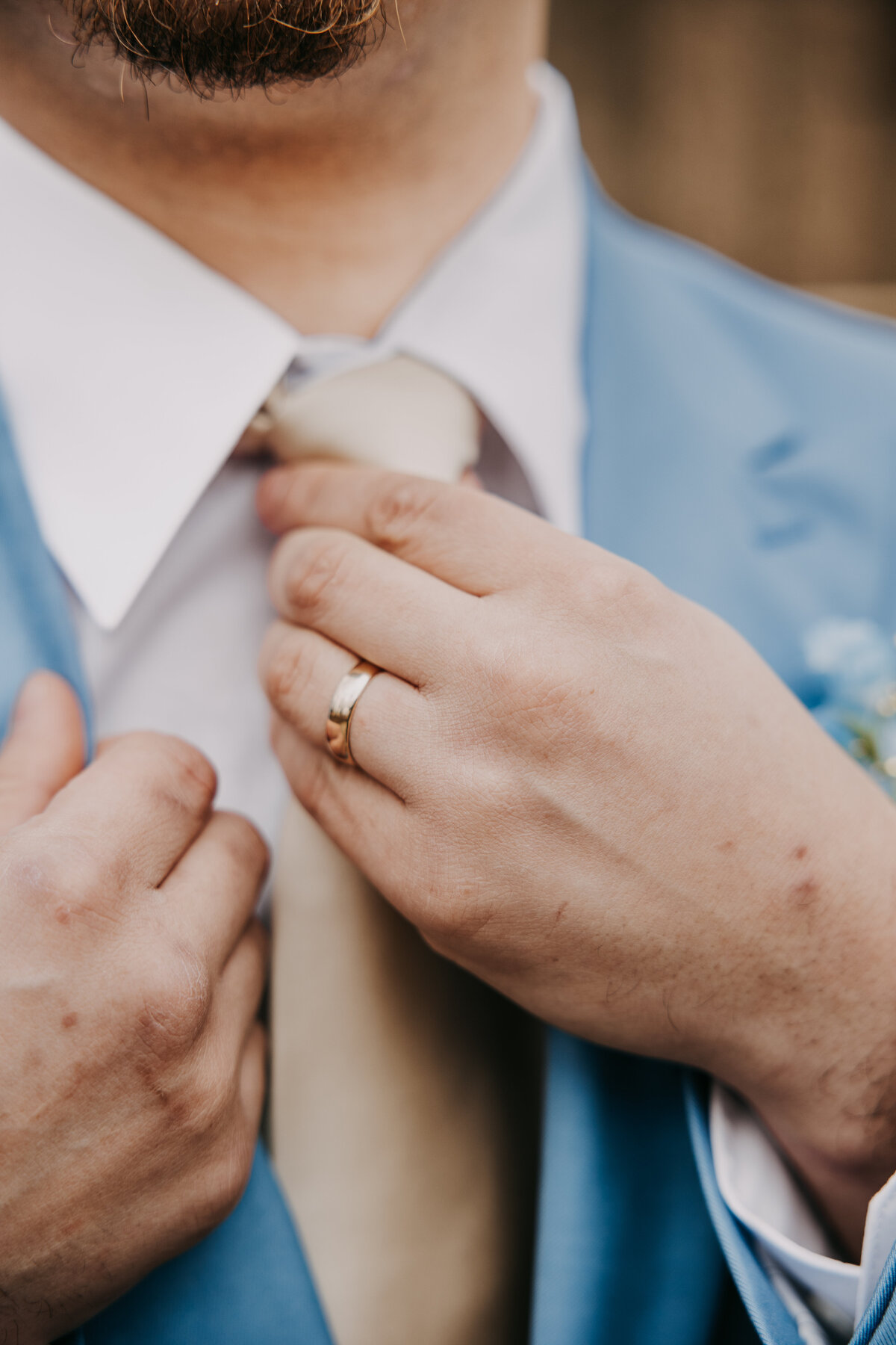 Close-up shot of the groom in a blue suit at Kincaid Manor, adjusting his tie with a focus on his wedding ring.