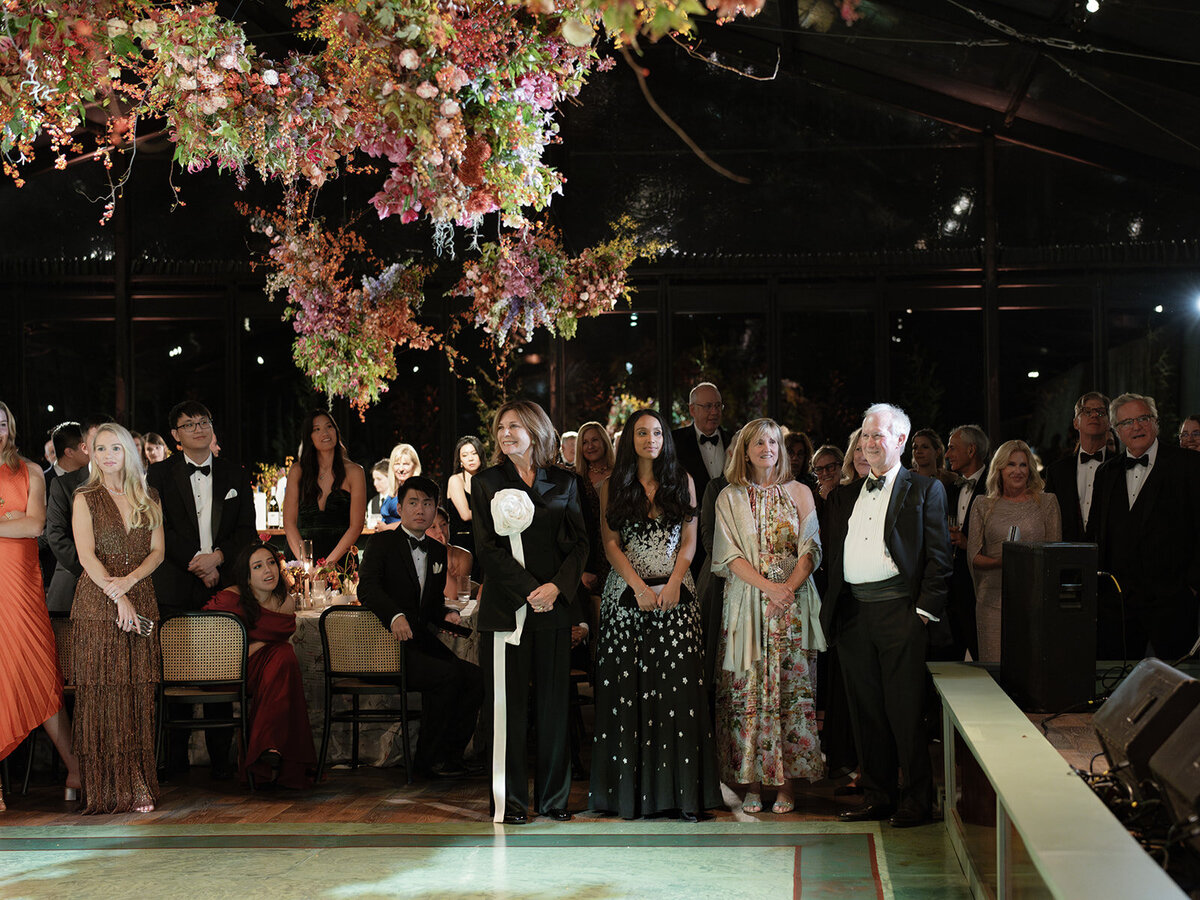 Interacting and sculptural floral clouds hang over the dance floor and bars of this fall wedding reception in Tennessee. Clear top tent build out for fall wedding reception in Tennessee hills.  Product clustered floral clouds in a tasteful fall color palette of copper, ruby, gold, burgundy, rust, and lavender. Orchids, bittersweet berries, butterfly ranunculus, and tulips are highlighted. Unique floral design with flower forward large scale installations. Design by Rosemary & Finch Floral Design in Nashville, TN.