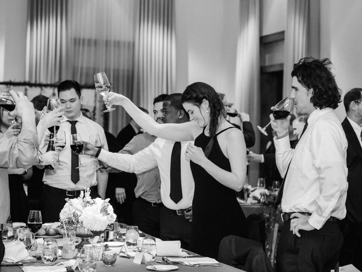 A black and white candid photo of guests toasting to the newlyweds