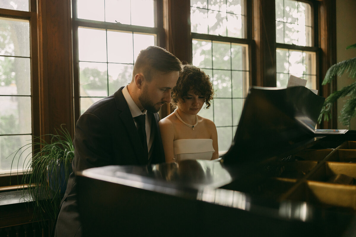 a groom and his bride sit at a piano looking down to play it