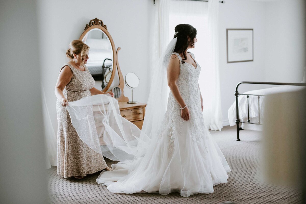 Bride in bridal suite getting ready before her London, Ontario wedding. Her mom is adjusting her veil behind her.