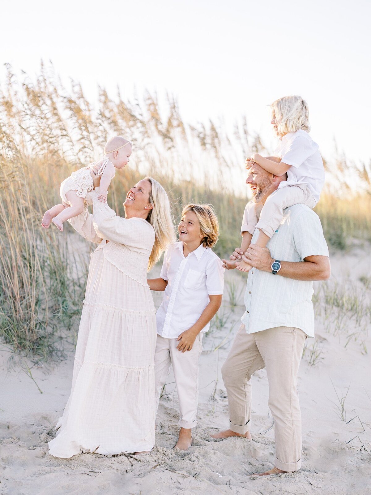 Two parents and three kids laughing together on the beach.