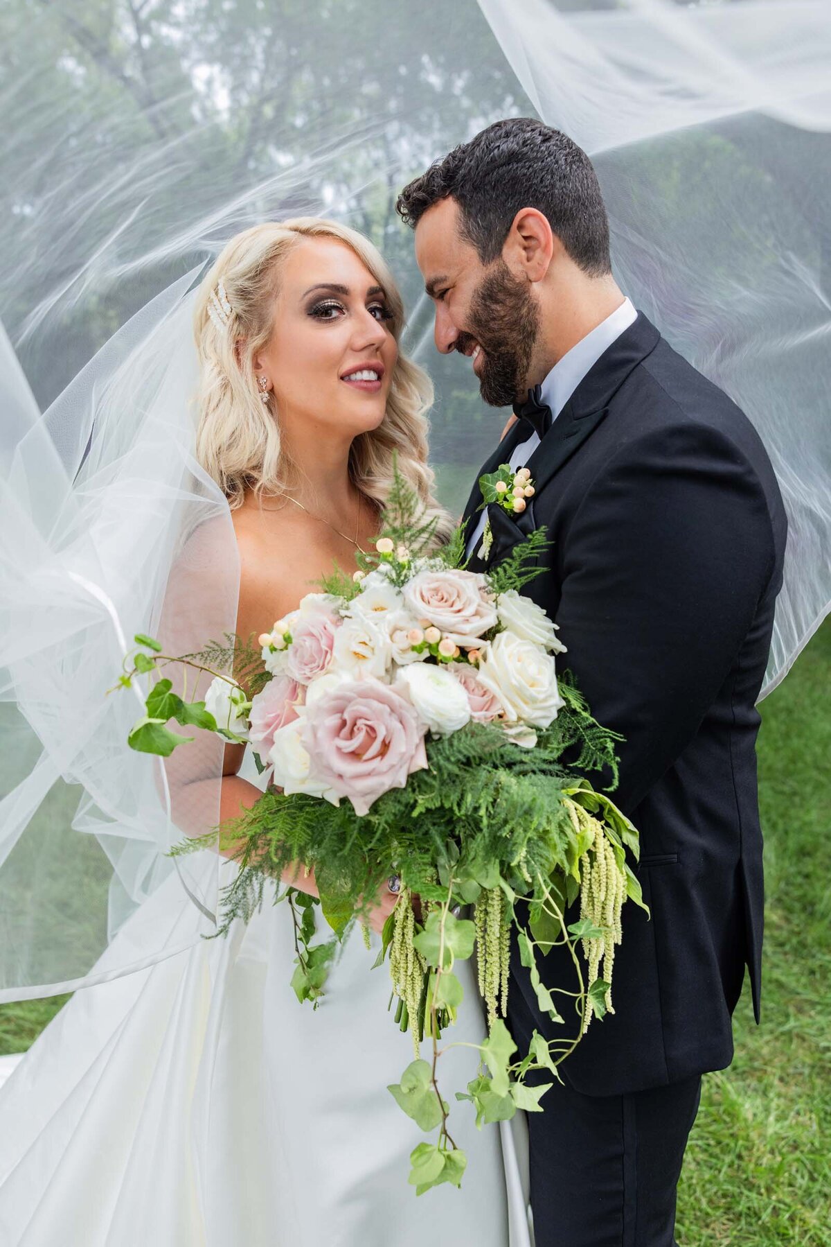 groom-smiling-at-bride-floral-arrangement-roses-veil