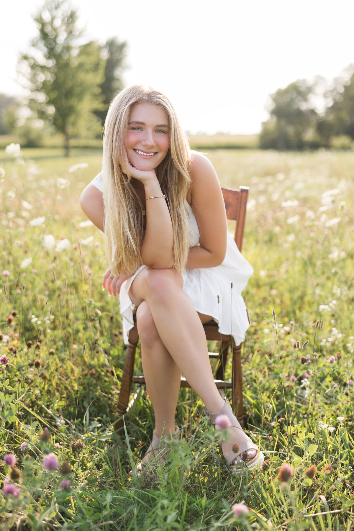 Senior girl seated on a chair in a field smiling at the camera