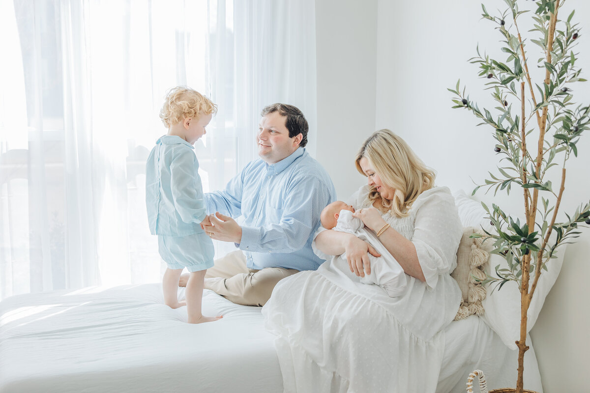 newborn photo with mom dad and big brother sitting on bed