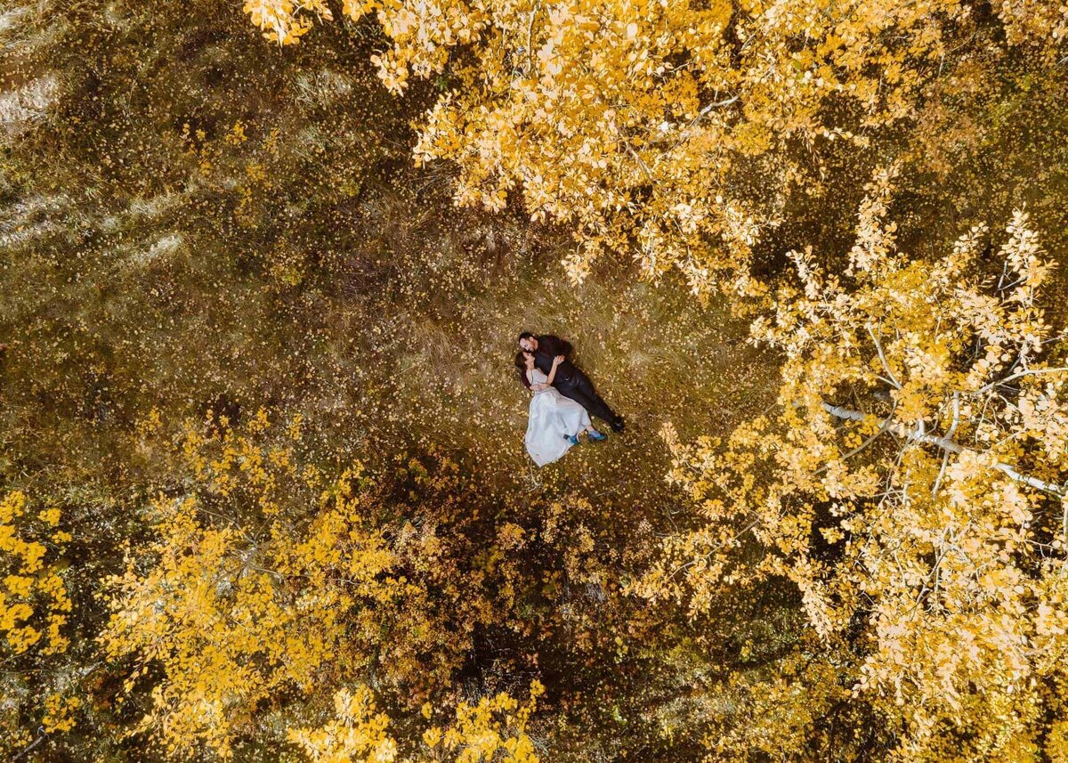 Aerial view of bride and groom lying on the ground surrounded by golden autumn aspen trees in Boulder, Colorado.
