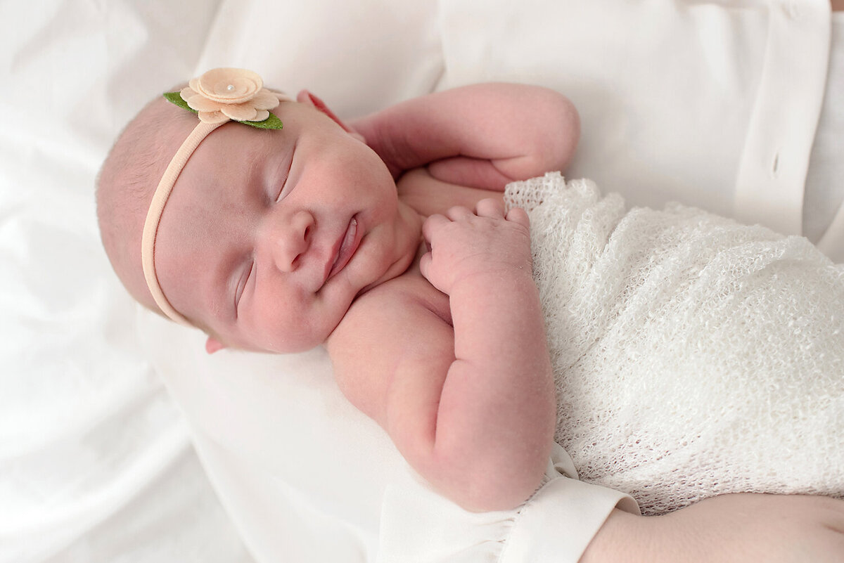 A brand new baby girl wrapped in a white swaddle and smiling while sleeping.