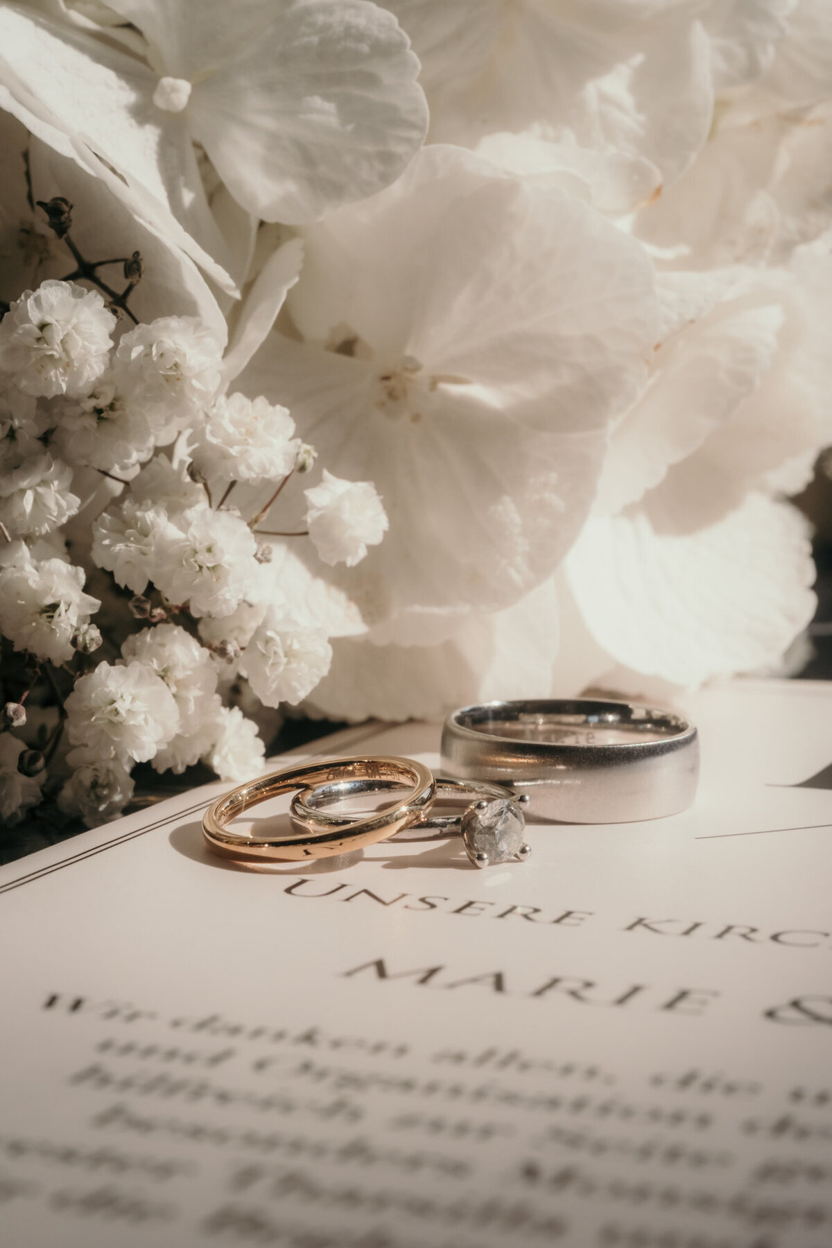 Detailshot of the wedding rings, white flowers and stationery.