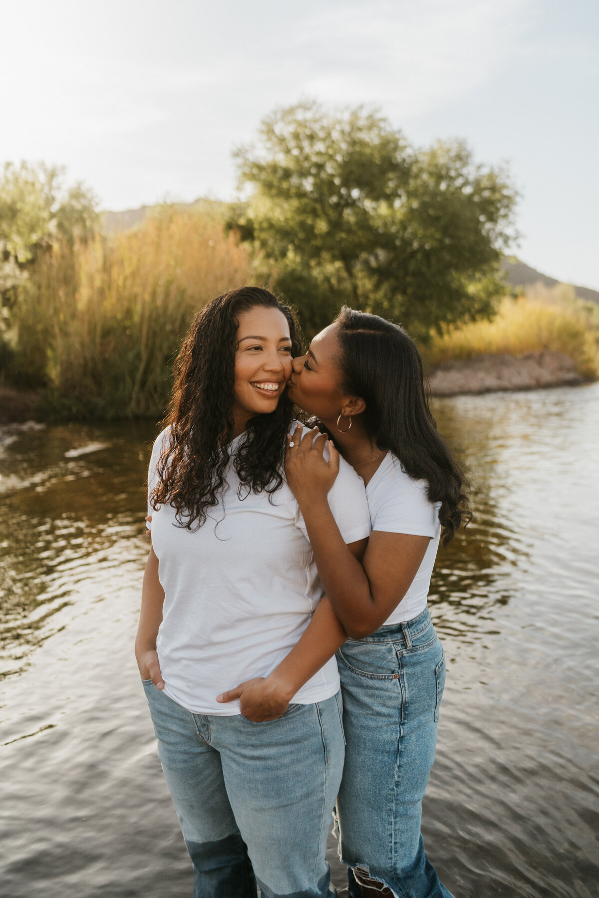 A person standing behind their partner and kissing their cheek 
