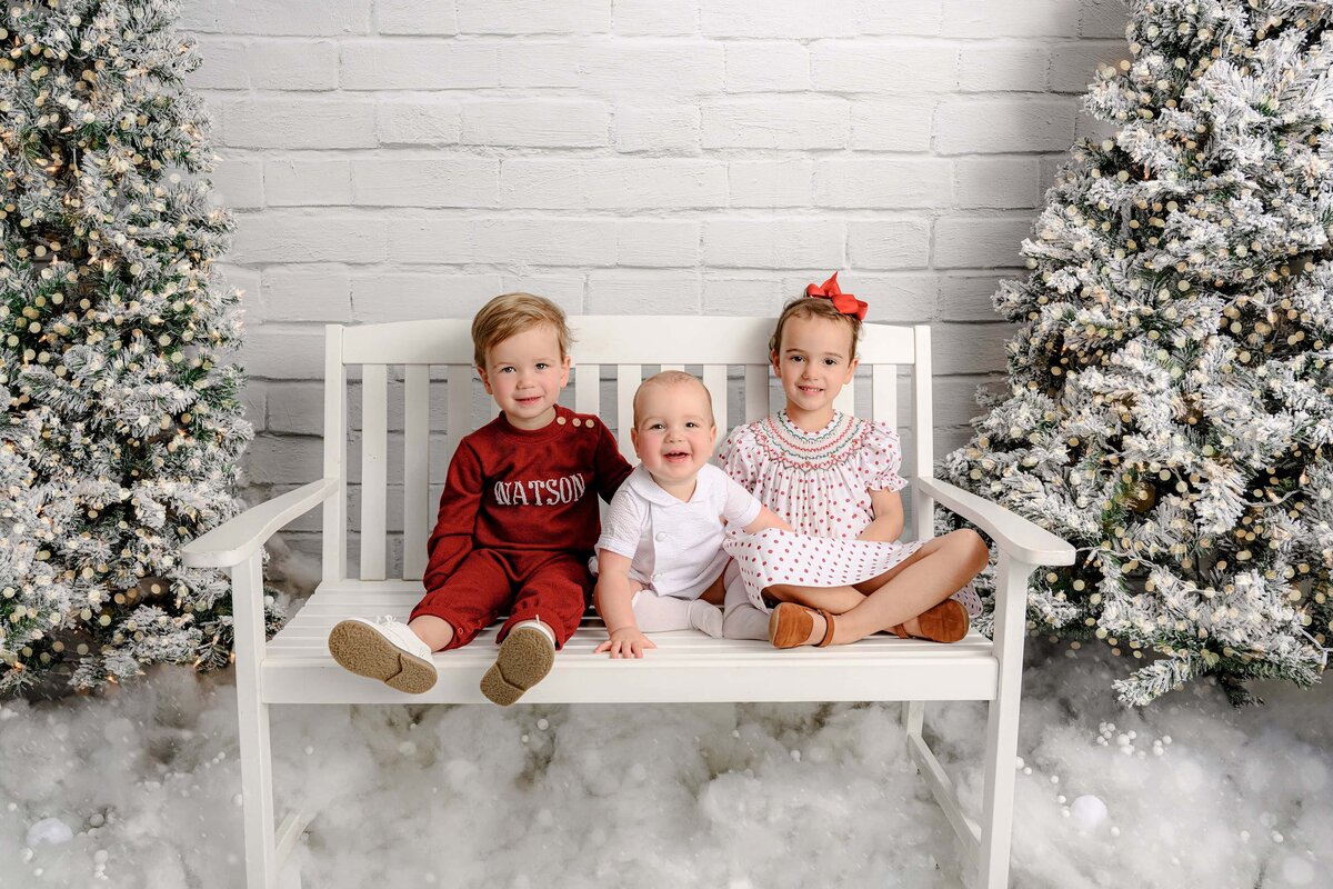 siblings sit on a white bench during white christmas holiday set up