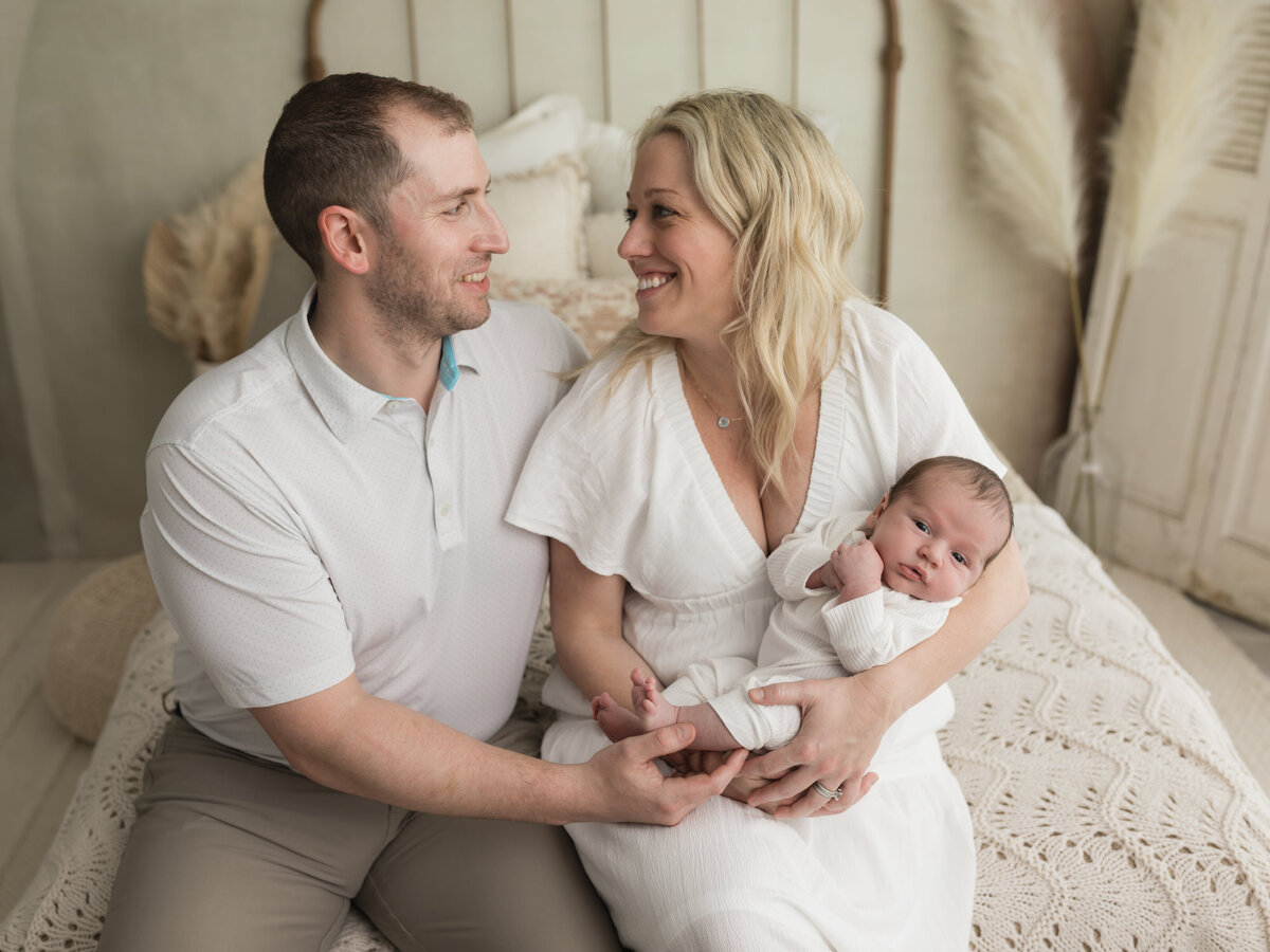 mom and dad holding newborn baby boy in white onesie for studio lifestyle session 