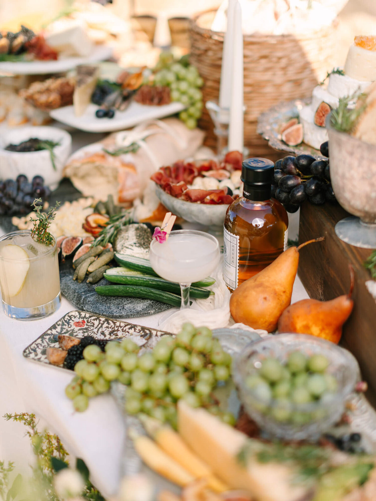 A lavish table spread featuring cheese, grapes, sliced bread, figs, pears, and cocktails.