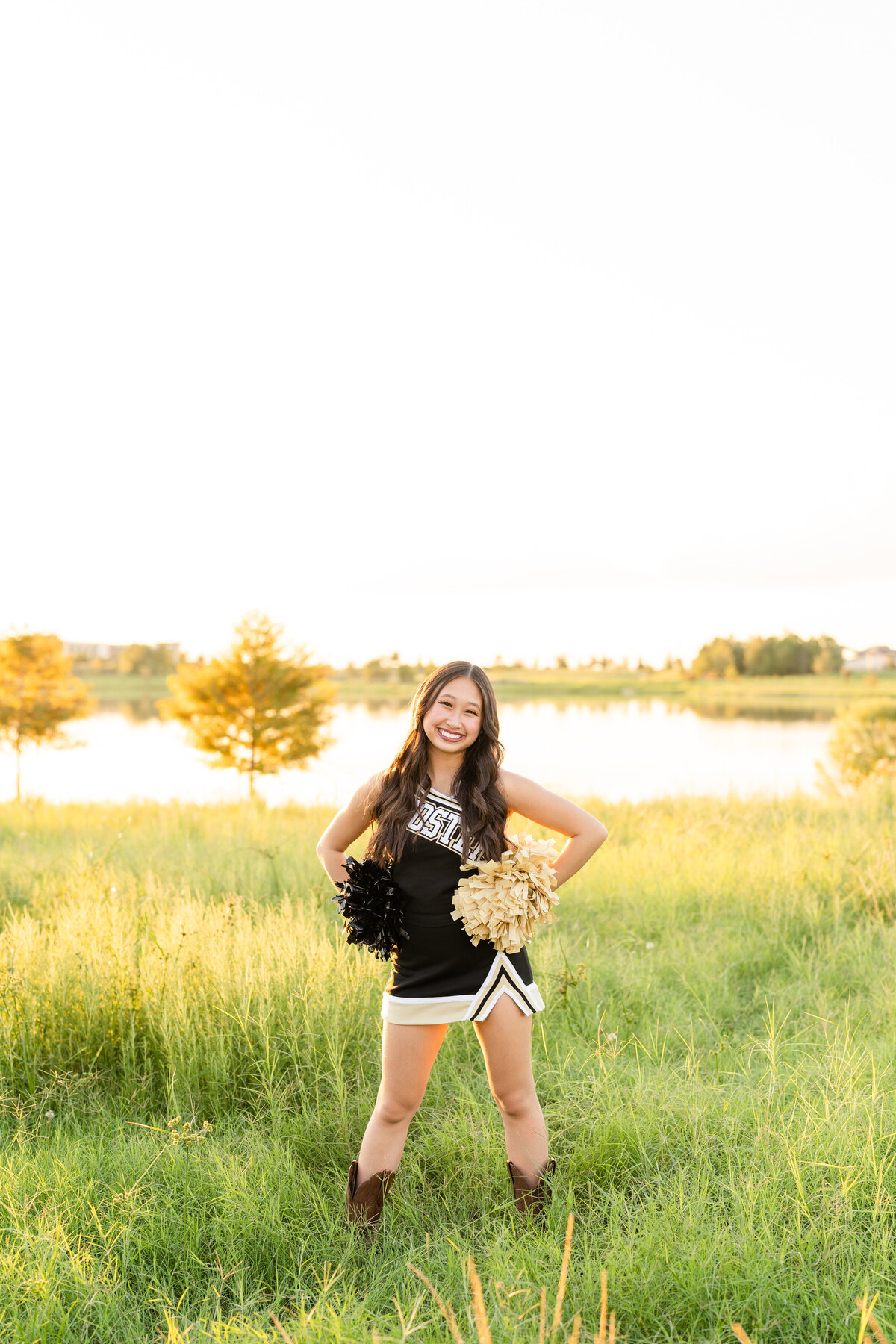 Houston high school senior girl wearing cheerleading outfit and holding poms in field by land and smiling at Josey Lake Park