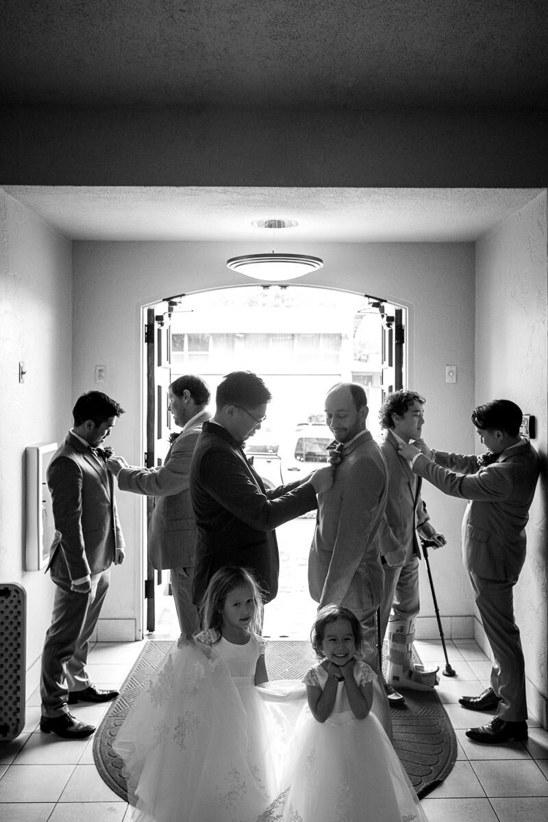 The groom and his groomsmen share a heartfelt moment as they help each other pin boutonnieres before the wedding ceremony at the beautiful Queen of All Saints Church in Concord, California.