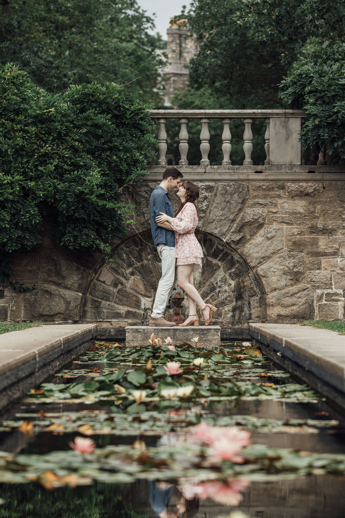 Couple by water lilies pond during spring engagement photo at New Jersey Botanical Garden in Ringwood New Jersey