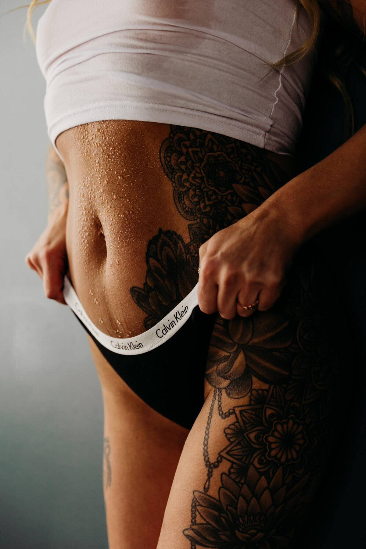 close image of a woman pulling up on her calvin klein thongs as water drips down her stomach below her wet white tank top