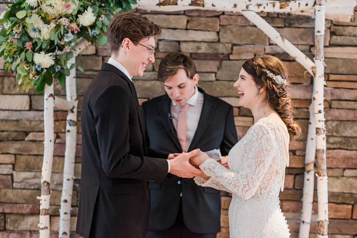 Bride laughs up at groom as they stand at the alter holding hands at their venue Boulder Wedgewood