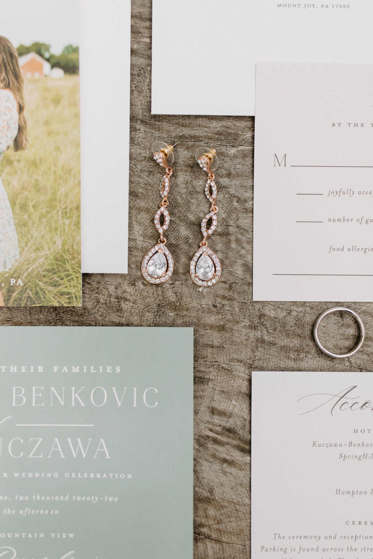 wedding invitations, earrings, and rings laid out on a wooden table