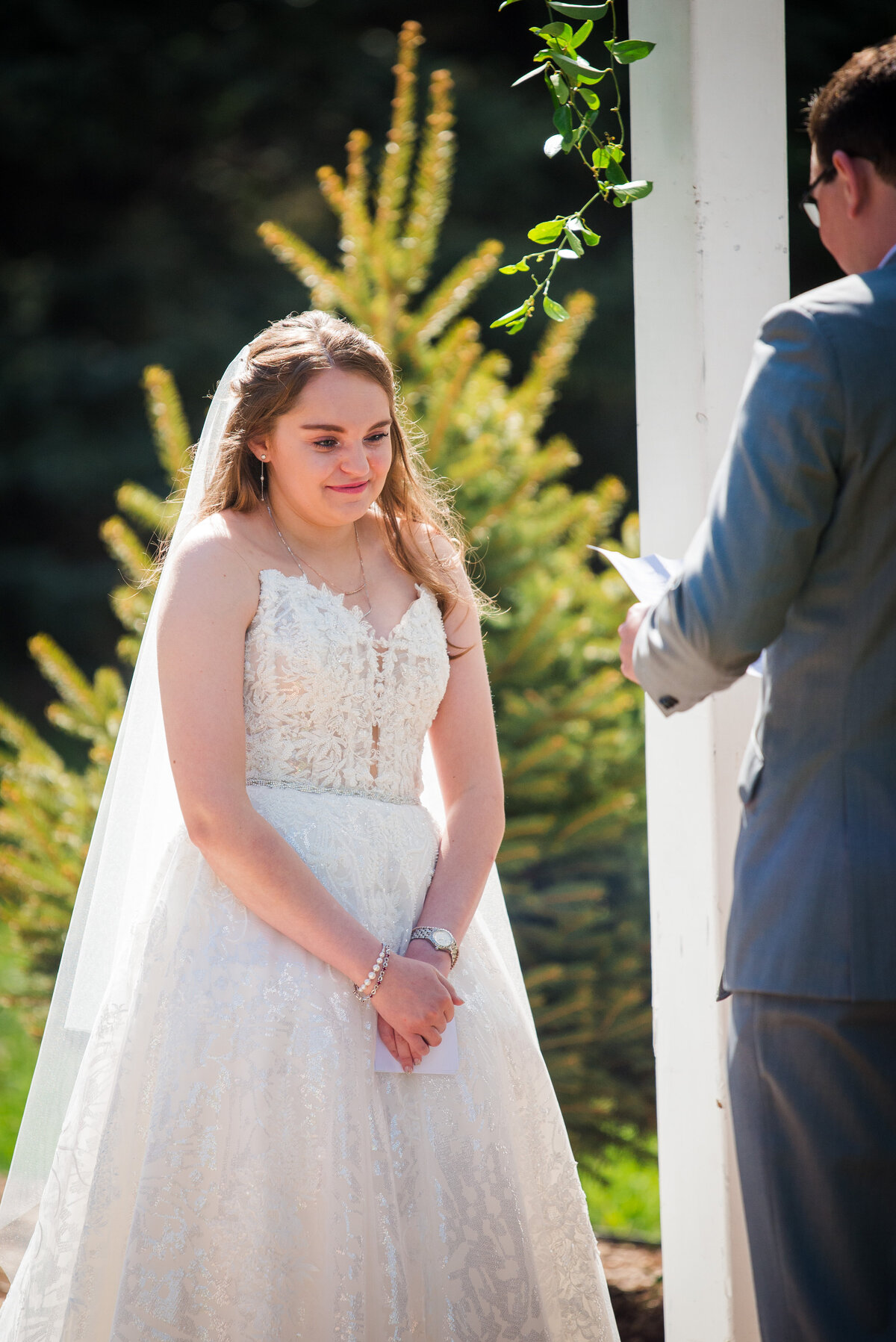 A bride looks emotionally as her groom reads his vows to her during their outdoor wedding ceremony.