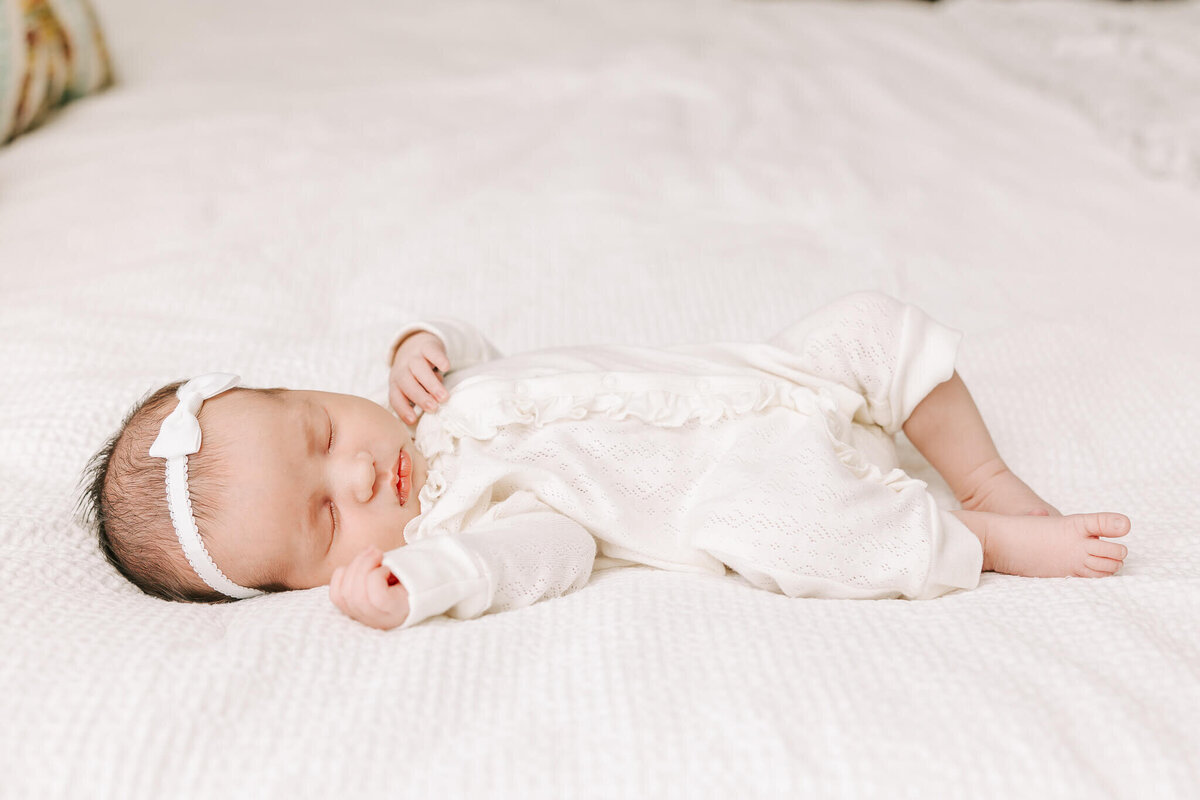 Baby girl wearing a a white outfit, sleeping through her newborn session with molly berry