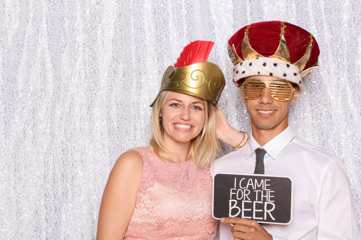 Couple pose together wearing silly hats in a photo booth at a wedding
