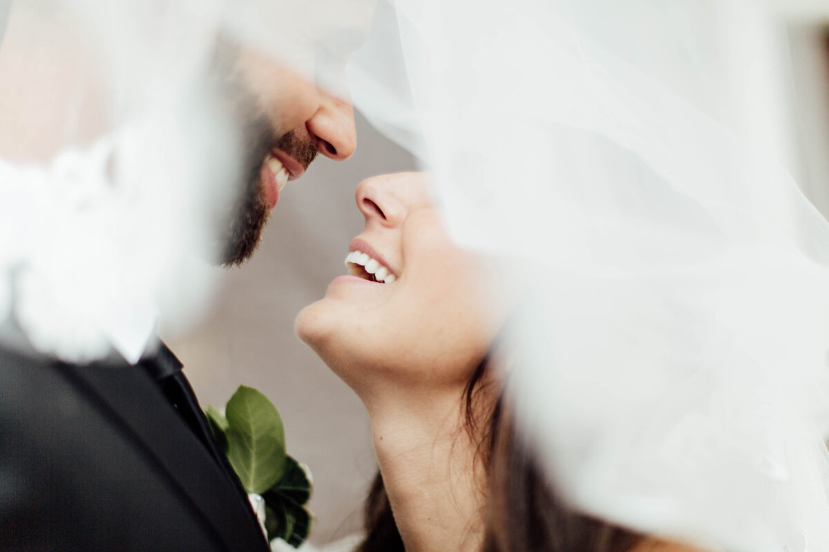 Groom and bride laughing under veil.
